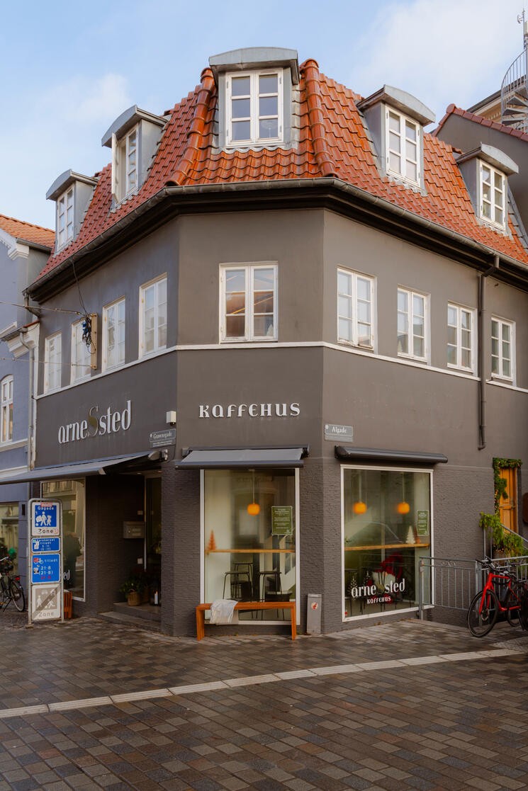 Exterior of the corner building housing Arnessted Kaffehus, with orange tiled roof, gray facade, and arnessted KAFFEHUS signage over the windows