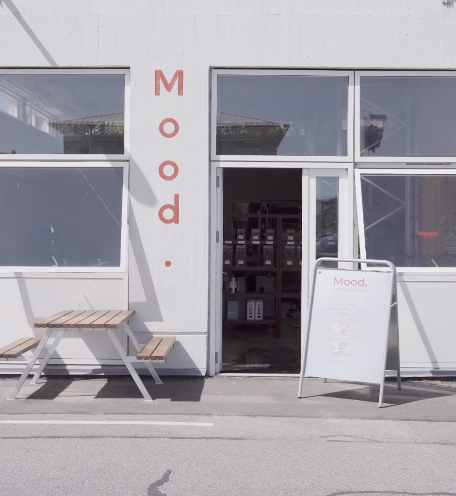 The white storefront of Mood Coffee Roasters with a picnic table and sandwich board out front