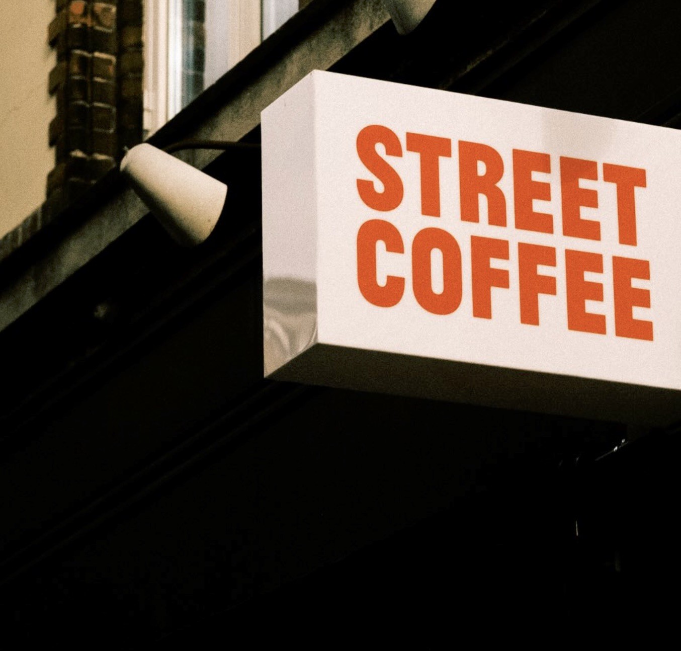 The Street Coffee storefront sign mounted at an angle beneath an awning, lettering in orange on white