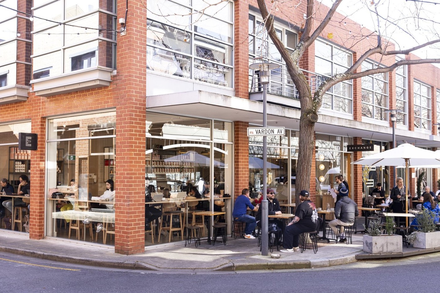 The Exchange Coffee corner shopfront on Vardon Ave, with the street sign, brick facade, and outdoor tables under umbrellas.