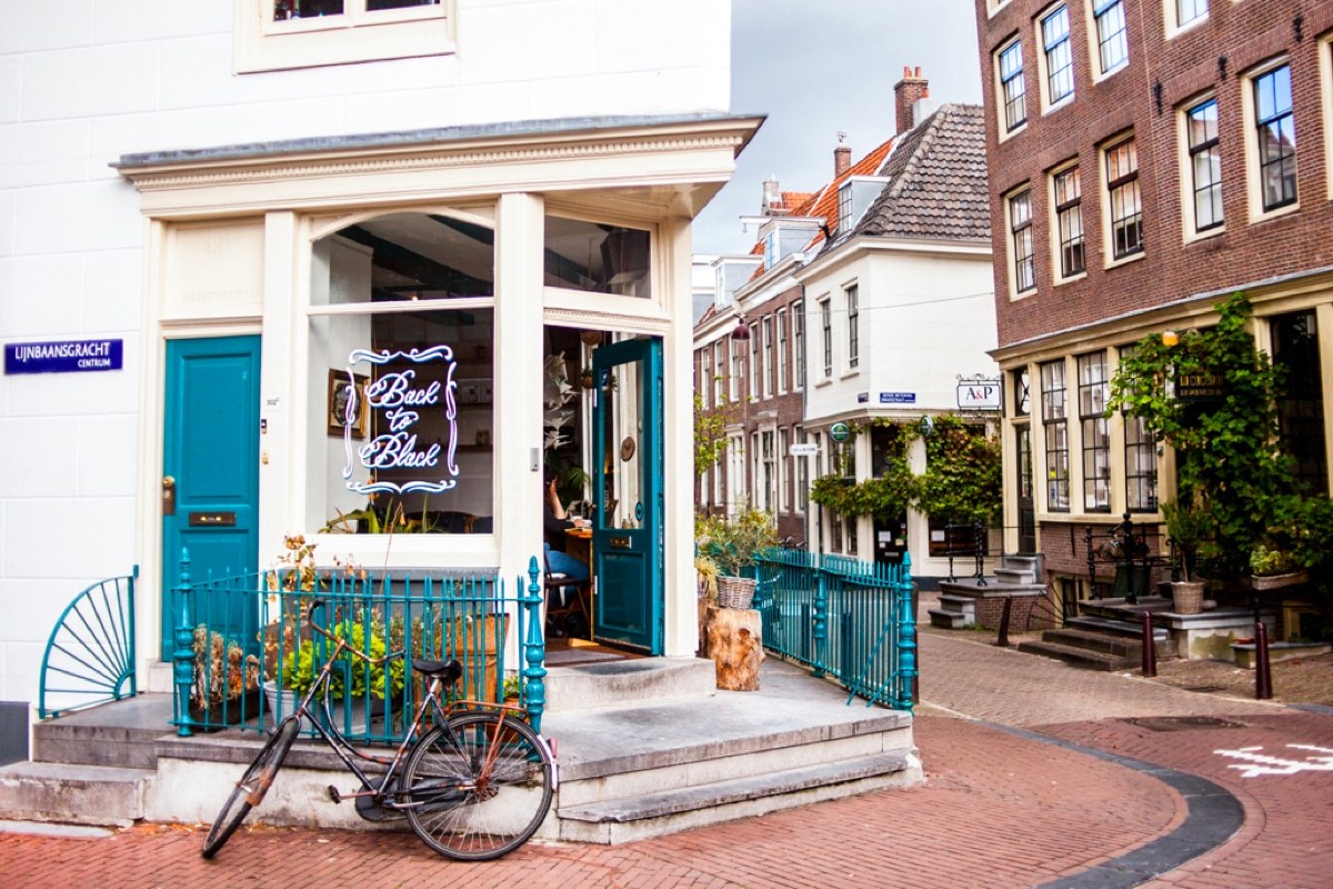 The teal corner storefront with a neon Back to Black sign in the window, a bicycle parked against the railing on the cobbled street