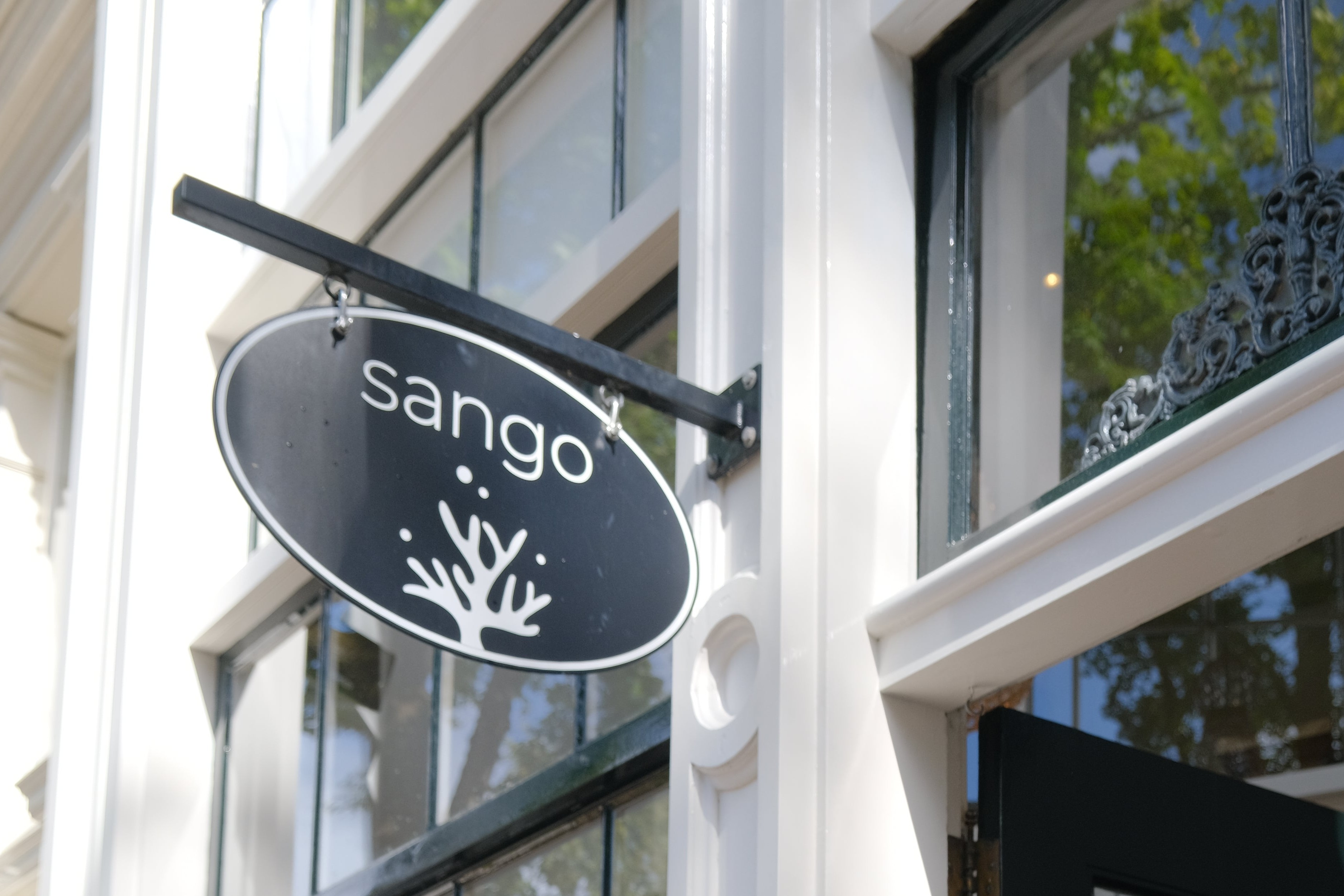 The oval black and white Sango sign hanging outside the shop's canal house facade in Amsterdam Centrum