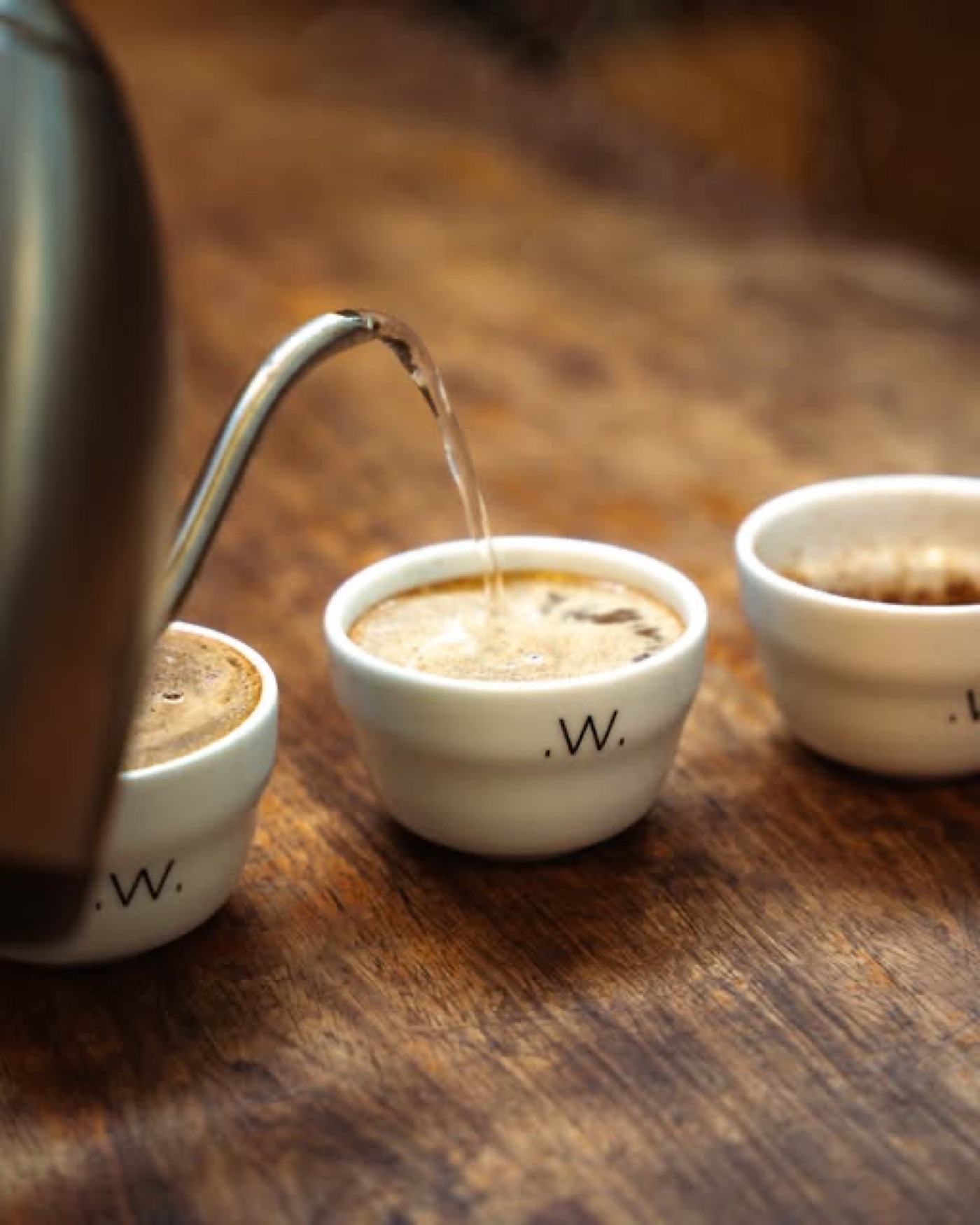Hot water poured into small White Label branded cupping bowls on a wooden table