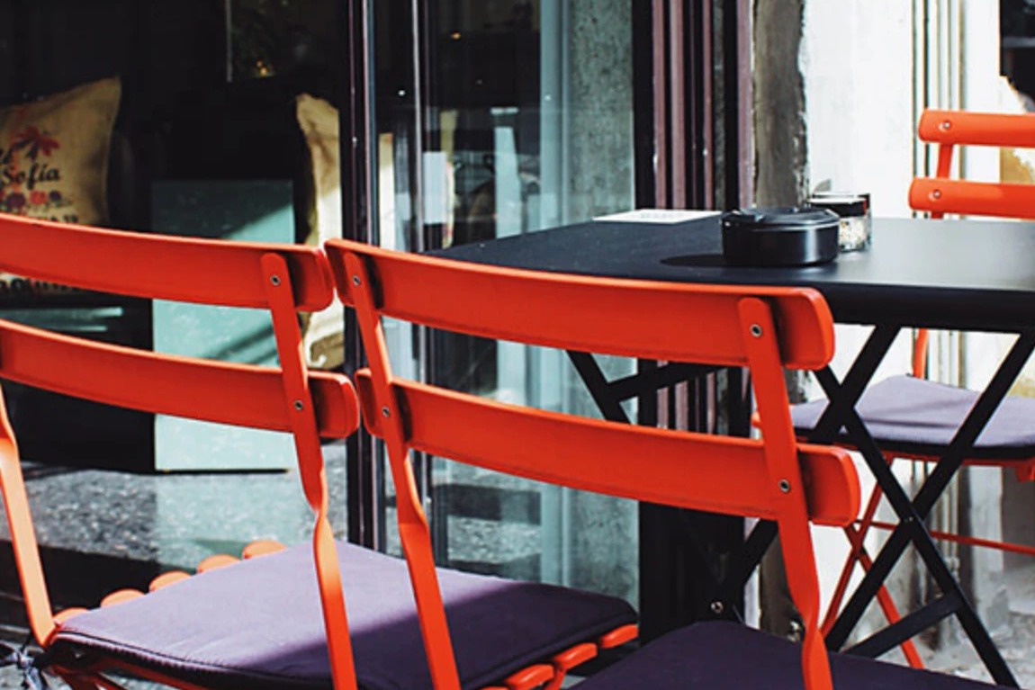Orange bistro chairs and a black table set up on Darg's outdoor terrace, glass doors reflecting the street behind