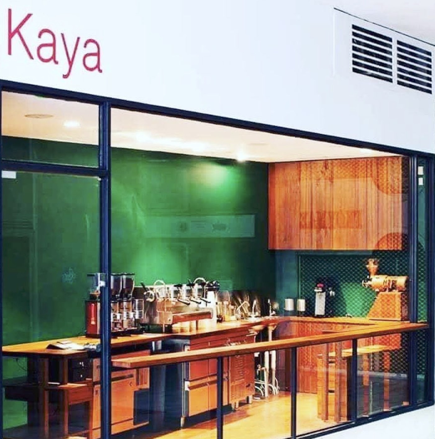 The green tiled Kaya storefront seen through glass, with the espresso bar and grinders visible inside