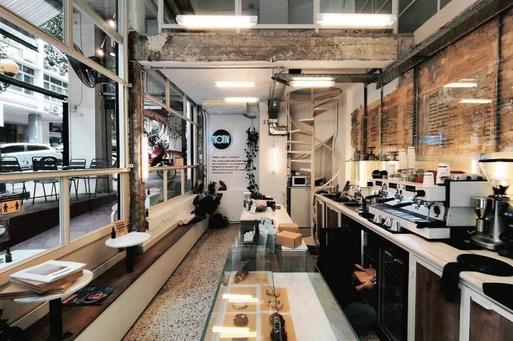 The long interior of MOTIV, terrazzo floor stretching past a spiral staircase to the espresso bar, with a neon MOTIV sign on the wall