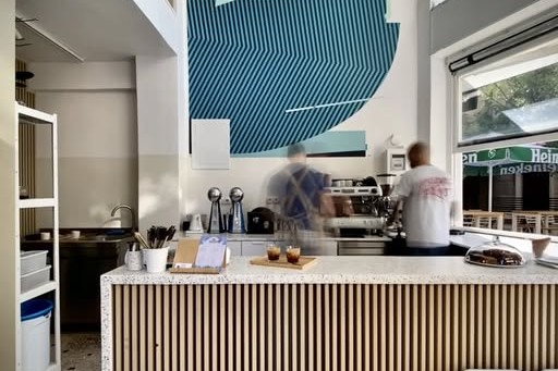 The terrazzo floored counter at Myller Coffee Shop with two baristas working the espresso machine beneath a blue geometric mural