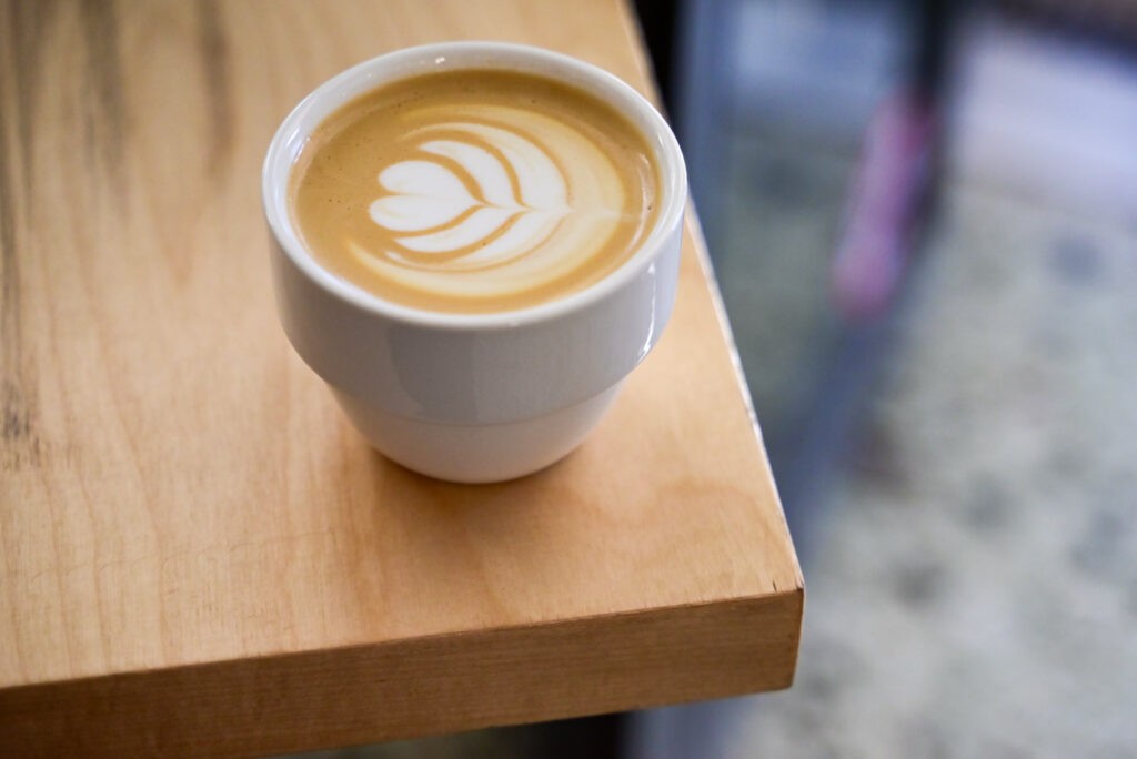 A cup of coffee with leaf pattern latte art on a wooden table at Omsom