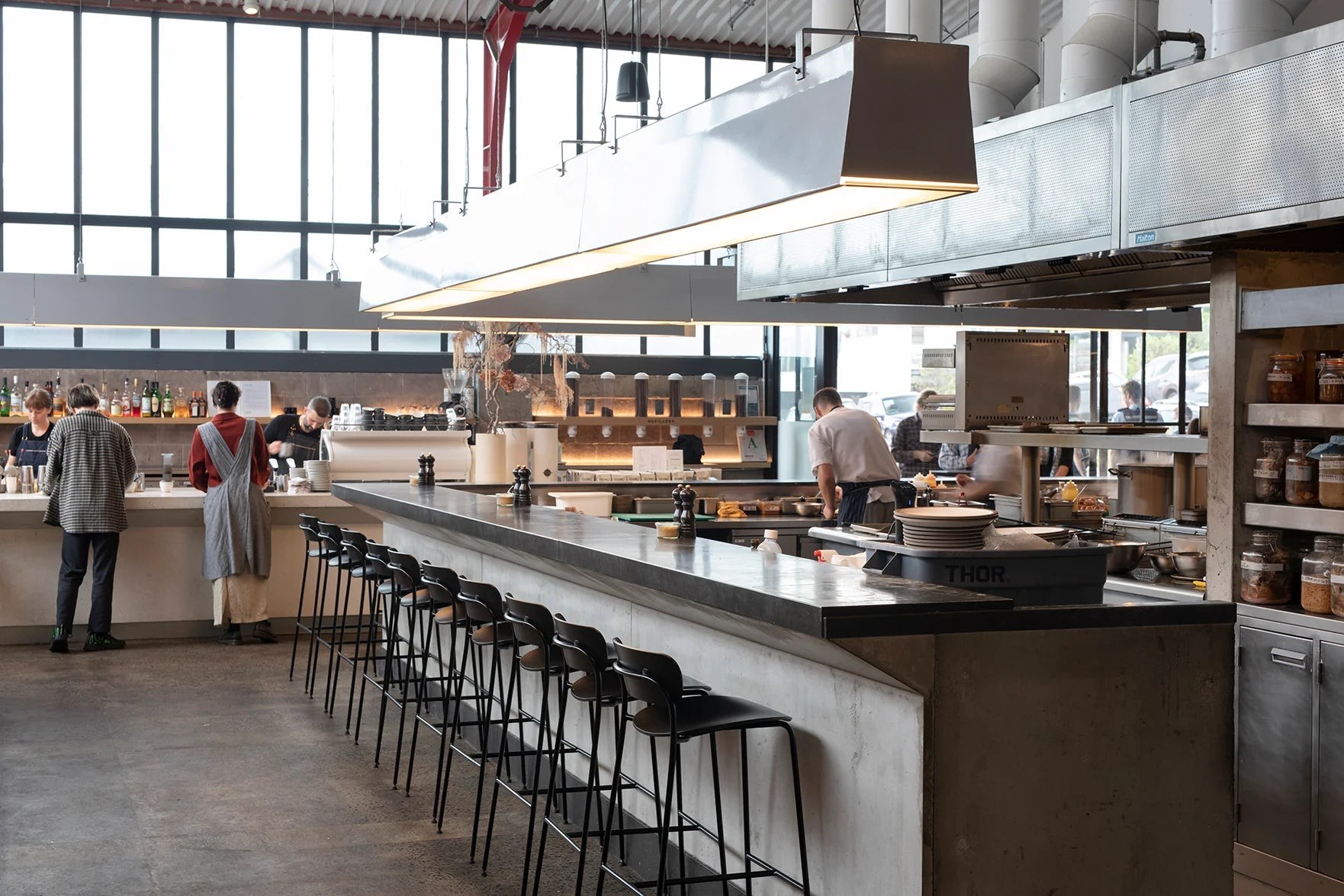 The open kitchen, long concrete and steel counter and tall steel framed windows inside Ozone Coffee Roasters in Grey Lynn