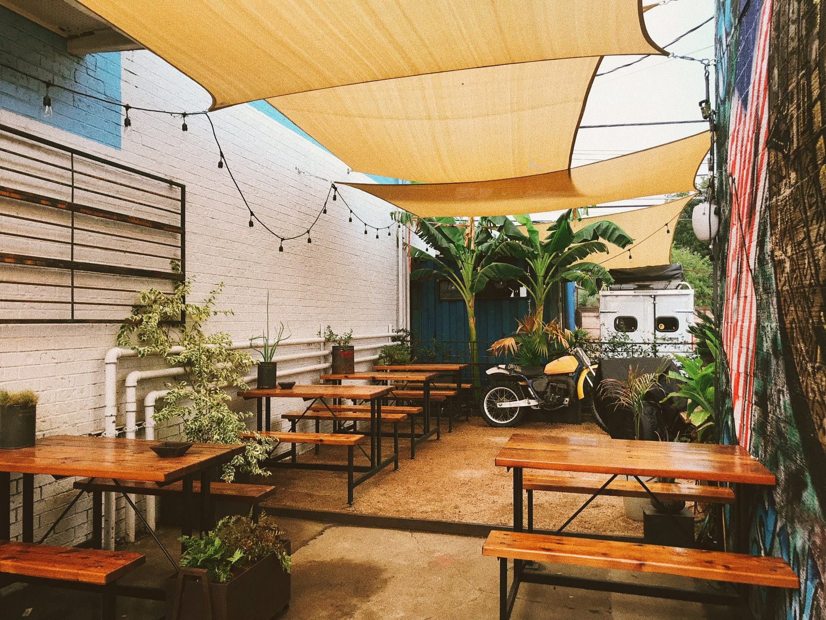 The shaded back patio at Flat Track Coffee with a motorcycle parked beside the mural wall