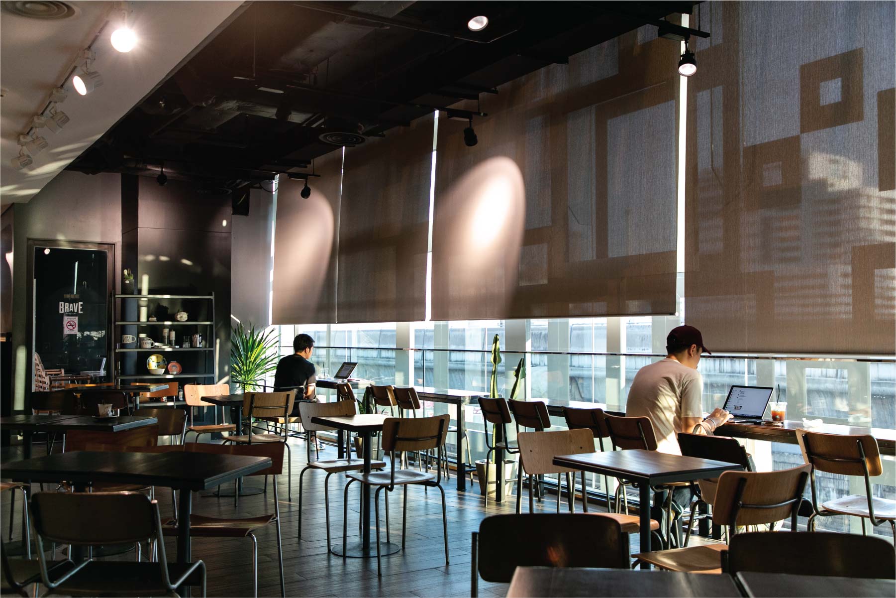 Brave Roasters' third floor room at Siam Discovery, people working at laptop tables by the window with a legible BRAVE sign on the glass door at left