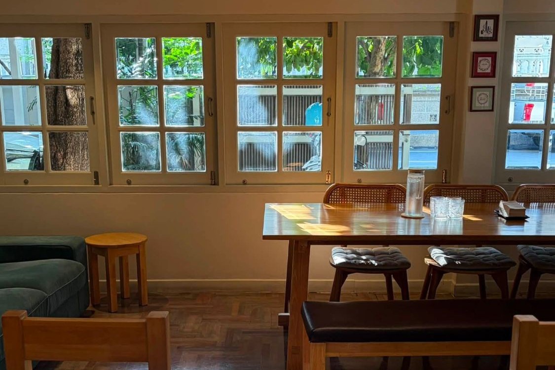 The sunlit dining room at Ceresia Coffee Roasters, a row of shuttered windows looking onto the trees outside, a long wood table with a water carafe and a green velvet sofa on a parquet floor