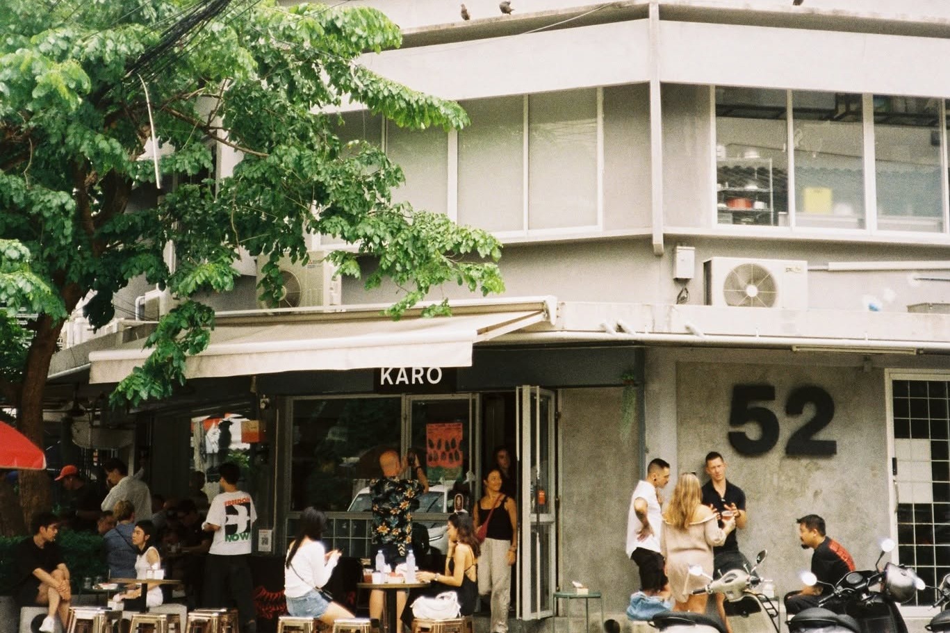 The Karo Coffee corner storefront on Pridi Banomyong 26, a legible KARO sign over the door and the building's 52 house number on the wall, people seated at outdoor stools