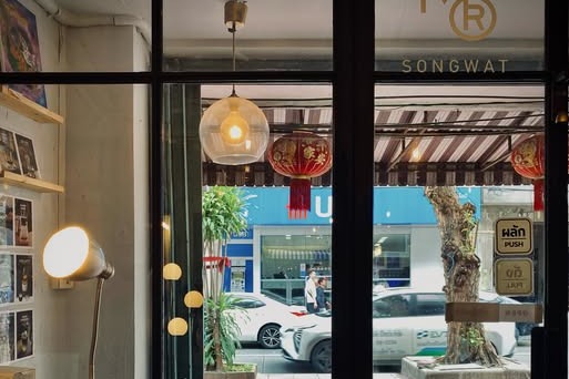 Looking through Mother Roaster Songwat's front window past a pendant lamp and red lanterns to the street outside, with a small MR SONGWAT logo in the corner