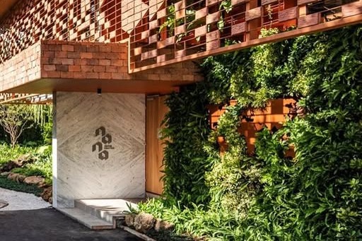 The checkered wood and brick facade of Nana Coffee Roasters Ari, with a carved nana logo on the stone entrance door and a green living wall beside it