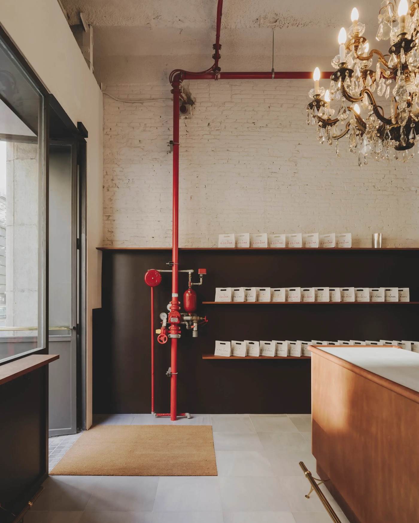 Coffee bags on open shelving beneath a crystal chandelier and red industrial pipe at NØMAD Cøffee