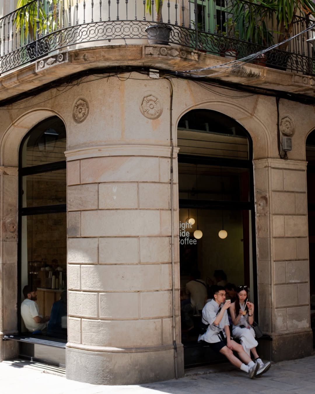 The stone corner building housing Right Side Coffee, its window lettering reading Right Side Coffee, with customers seated in the arched doorway