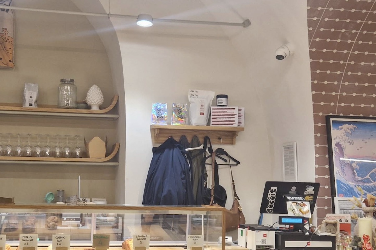 The counter at Cosmico with roasted bean bags on a shelf, a pastry case up front, and a framed Hokusai print on the wall