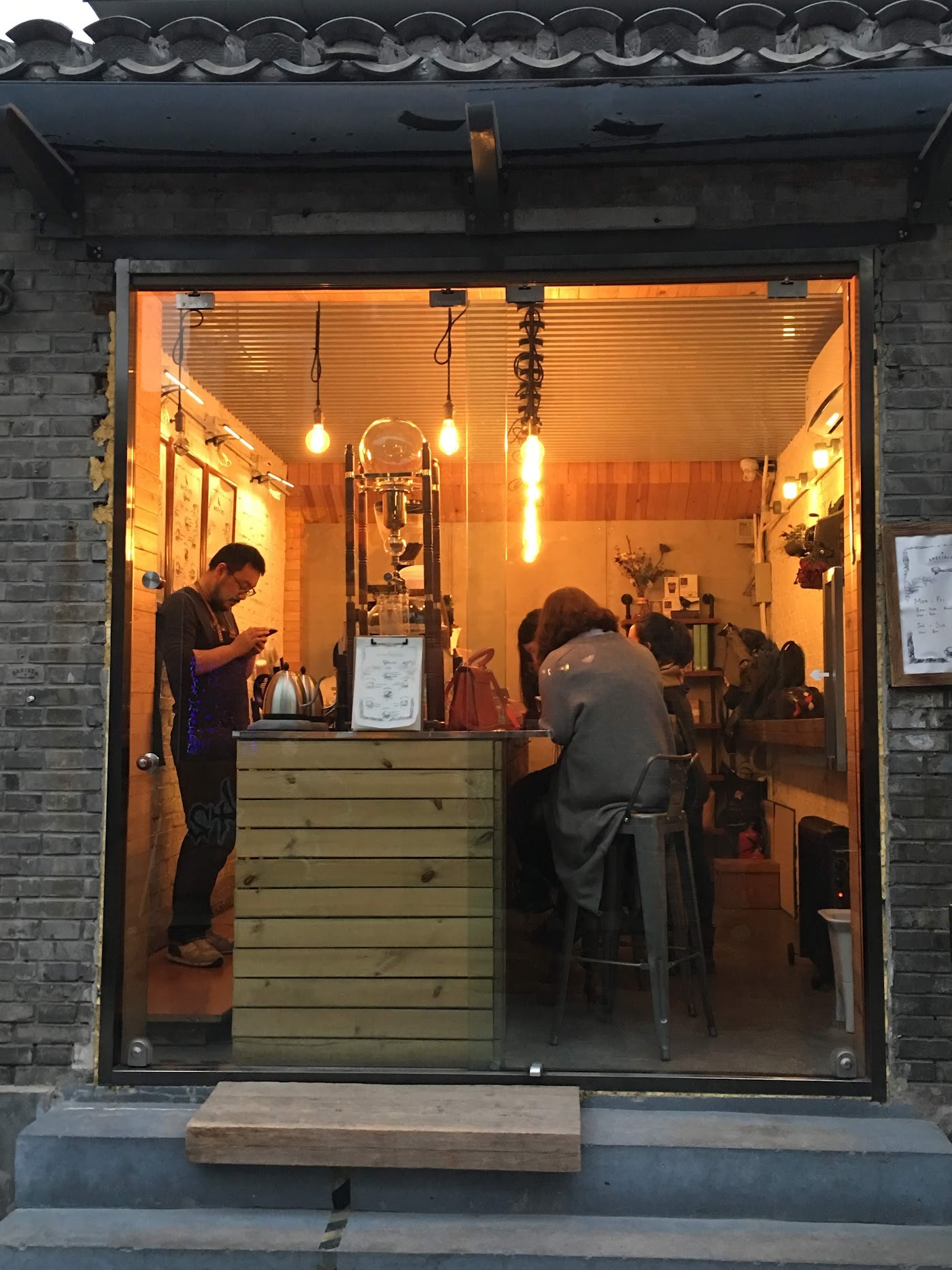 The lantern lit counter at Barista Coffee Roasters, a barista and seated customers visible through the glass storefront