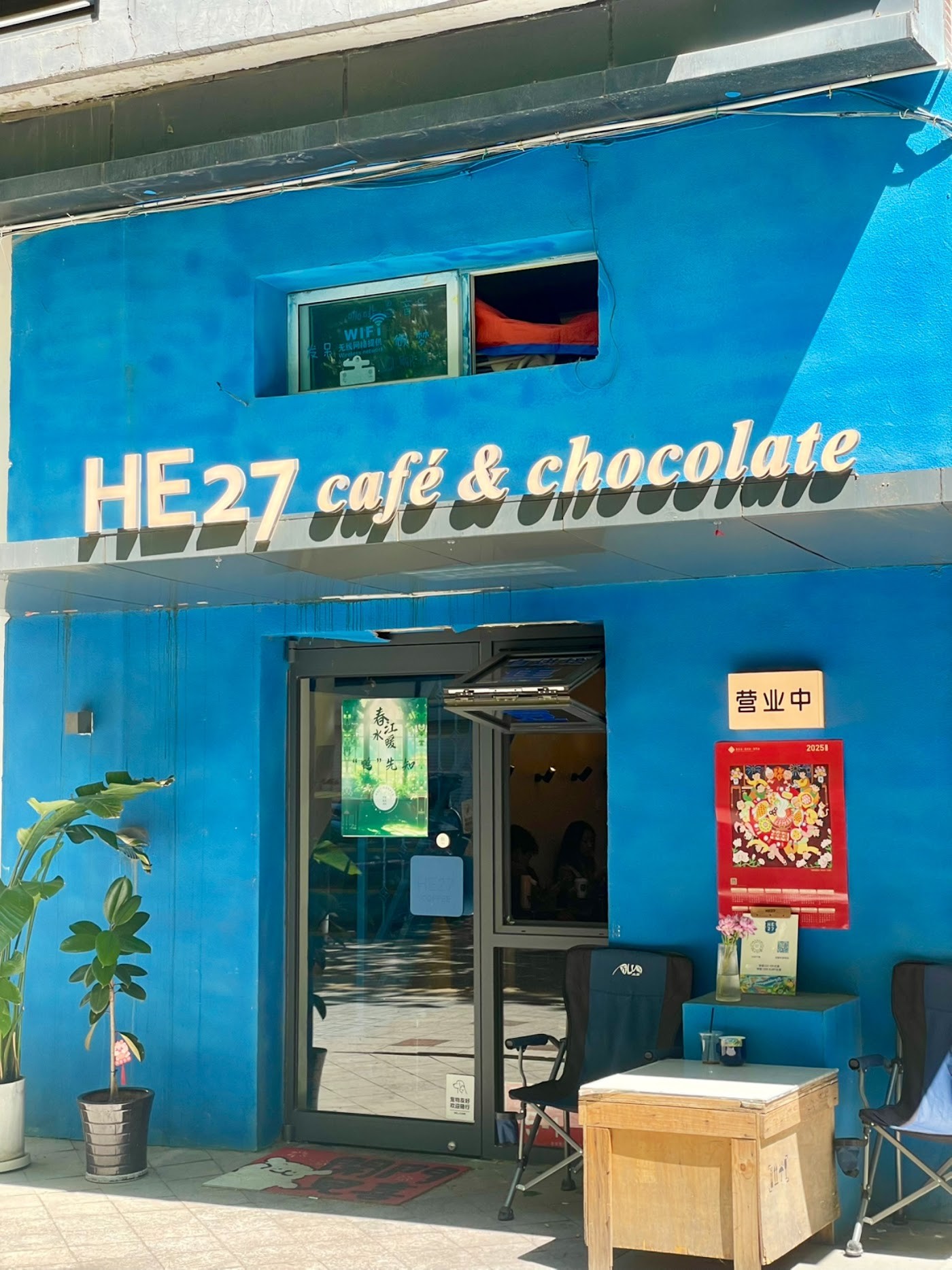 The bright blue He27 cafe and chocolate storefront with its illuminated sign and an open sign posted by the door