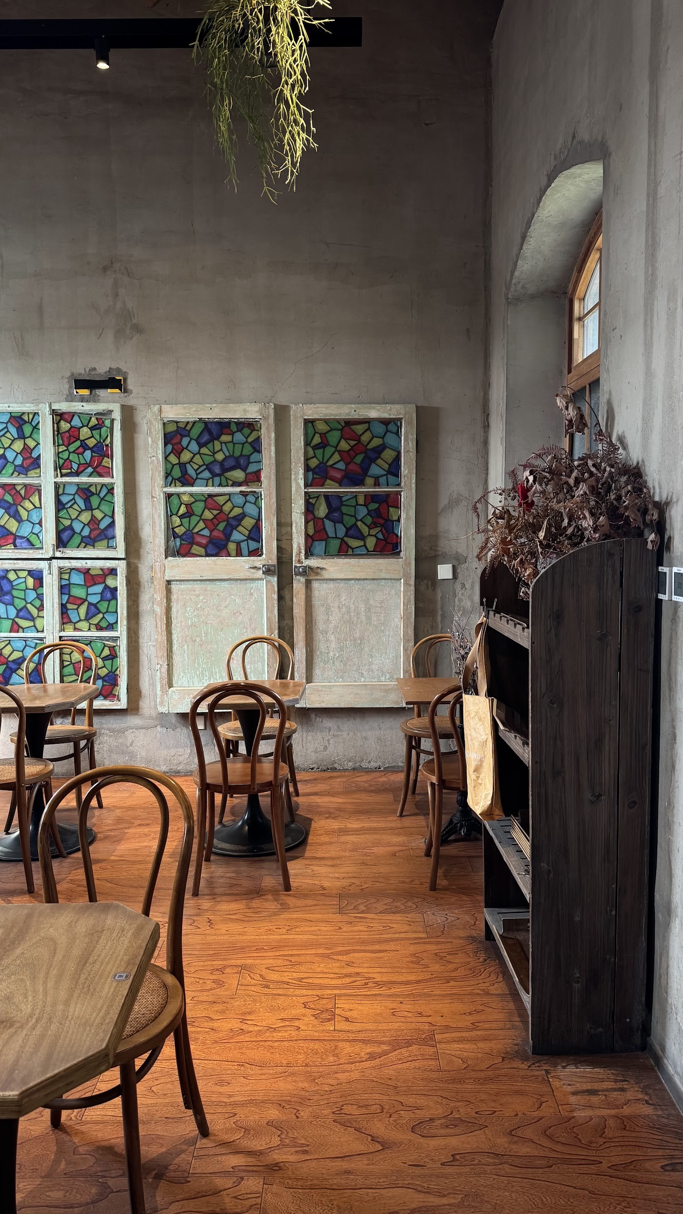 The empty dining room at Metal Hands with stained glass panels on the wall and bentwood chairs around small wooden tables