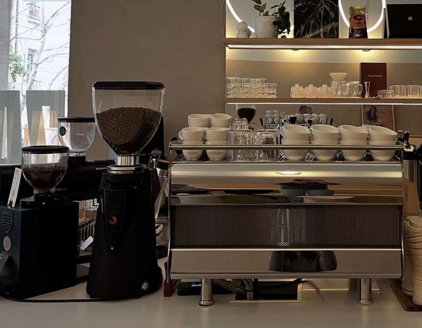 The espresso bar at 7AM Roasters with grinders, stacked cups, and a lit shelf of retail bags and glassware