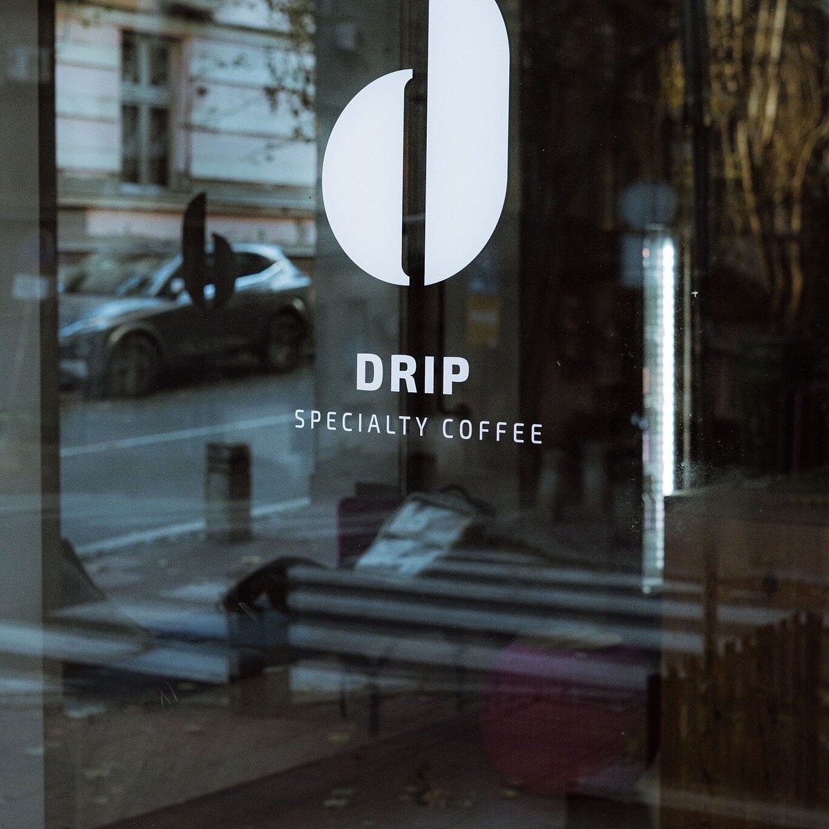 The DRIP Specialty Coffee logo on the glass storefront door, reflecting the street outside