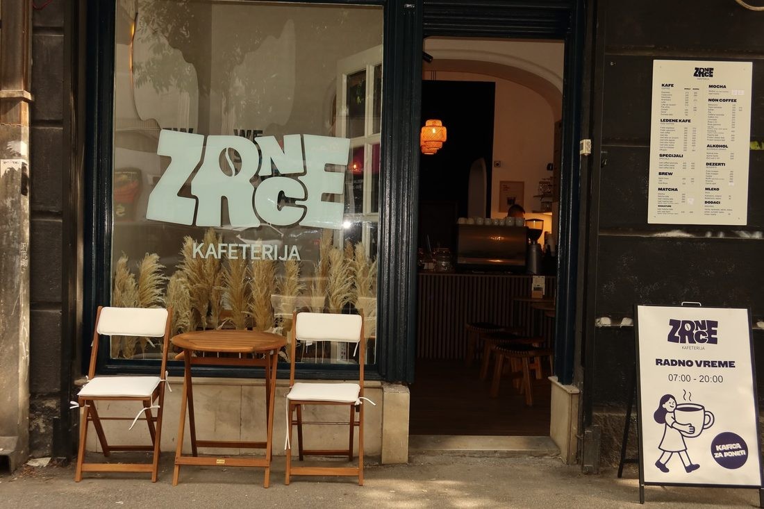 The Zrnce Kafeterija storefront with pampas grass in the window and outdoor bistro seating