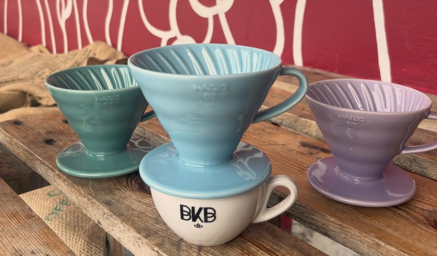 Three colorful Hario V60 drippers of different sizes lined up on a wooden crate at Bergen Kaffebrenneri