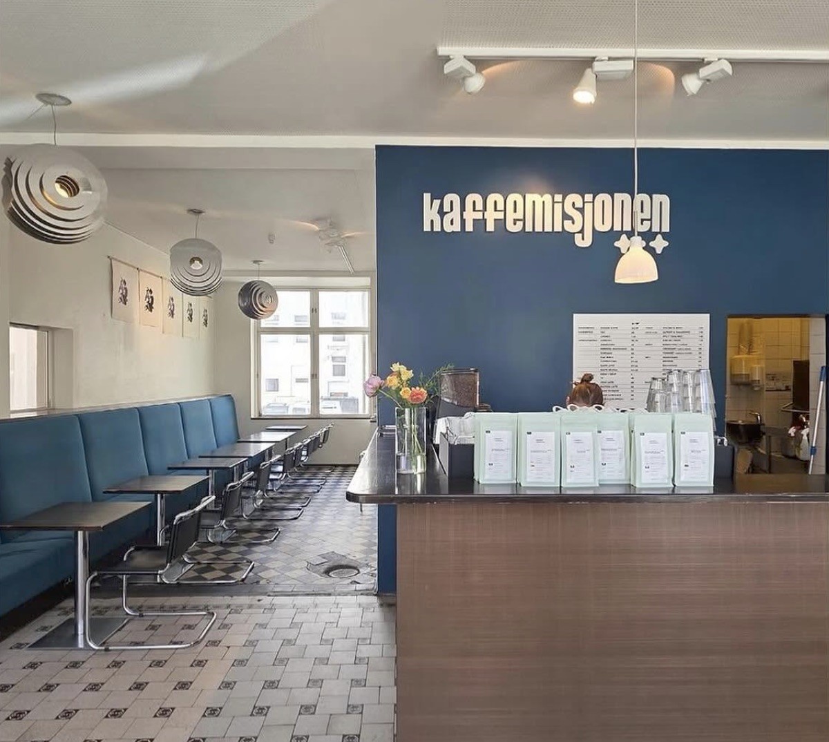 Rows of green retail coffee bags on the wooden counter beneath the Kaffemisjonen sign on a blue wall