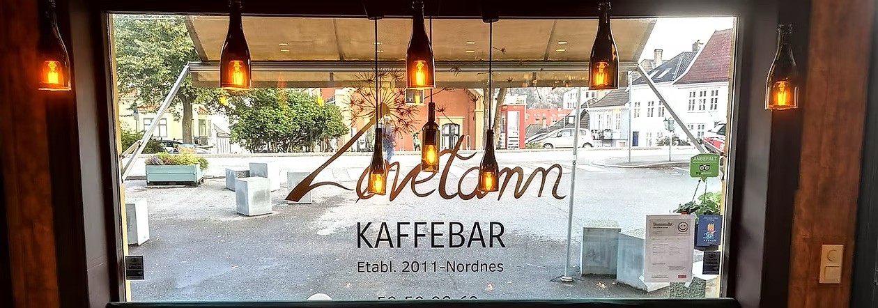 The Løvetann Kaffebar window lettering with hanging bottle pendant lights and a view of the Nordnes square outside