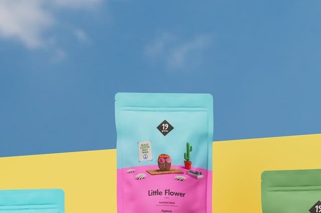 A pastel colored 19grams Little Flower retail coffee bag styled against a blue sky and yellow backdrop