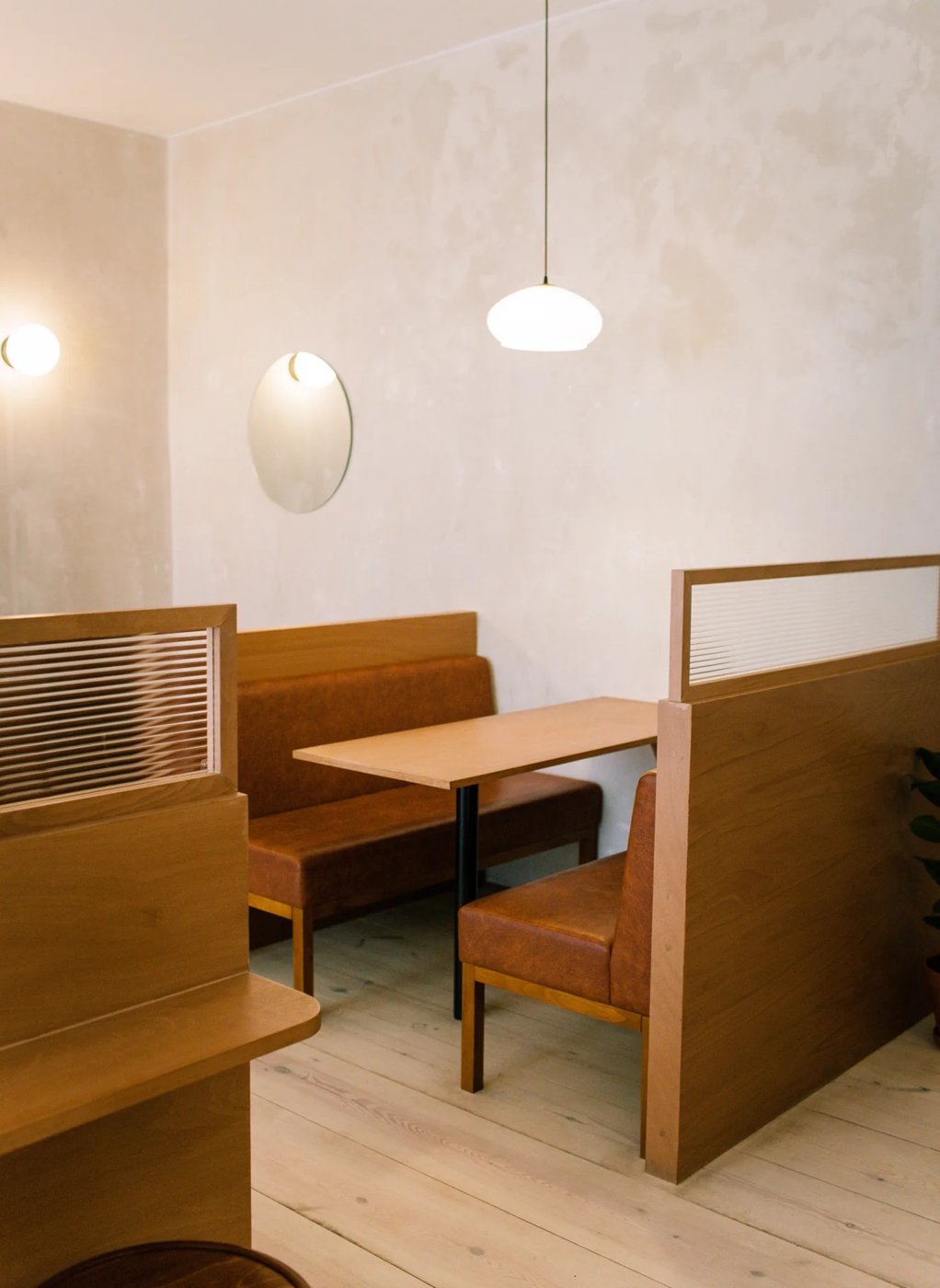 A booth seat at Companion, warm wood banquette and table, soft pendant light, plaster walls