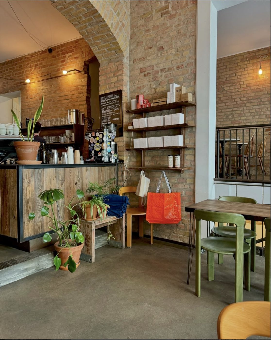 Distrikt Coffee's arched brick interior, plants and a tote bag on a bench, the counter visible under the arch