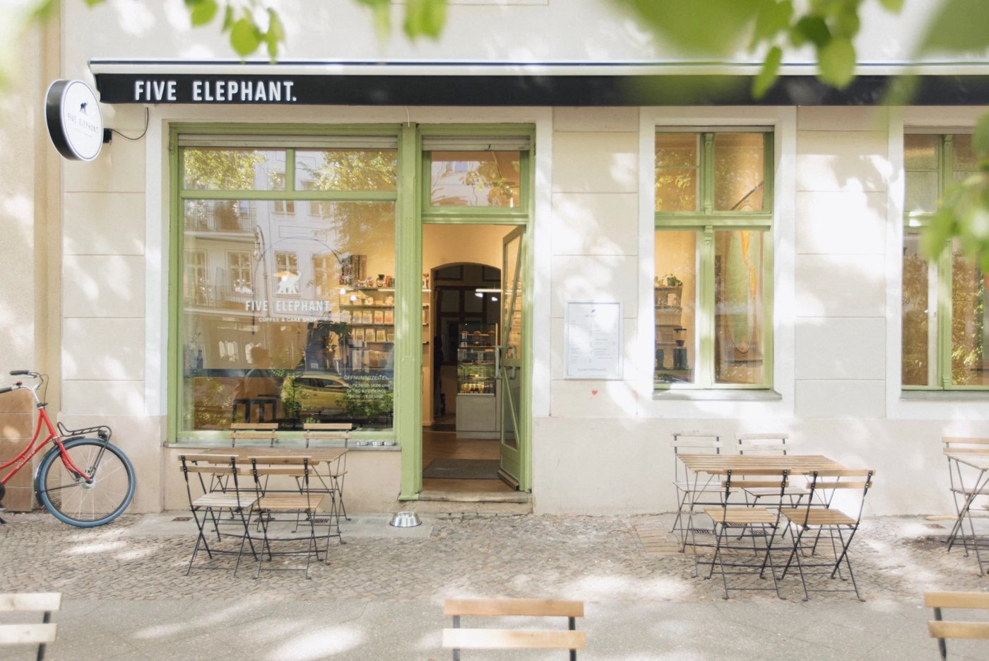 The green-framed storefront of Five Elephant, outdoor tables under trees, FIVE ELEPHANT signage above the door
