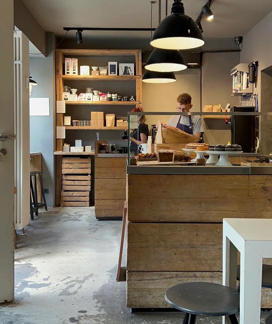 Inside The Barn, raw wood shelving stocked with bags and brewing gear, a barista working behind the pastry case