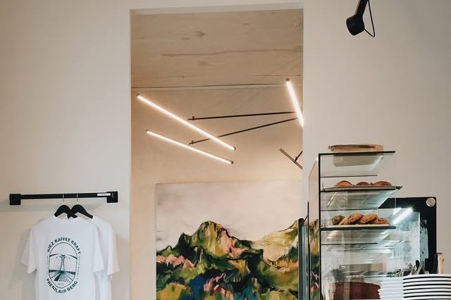 Interior of Kiez Kaffee Kraft with a branded t shirt on a rack, a landscape painting, and the pastry case in the background