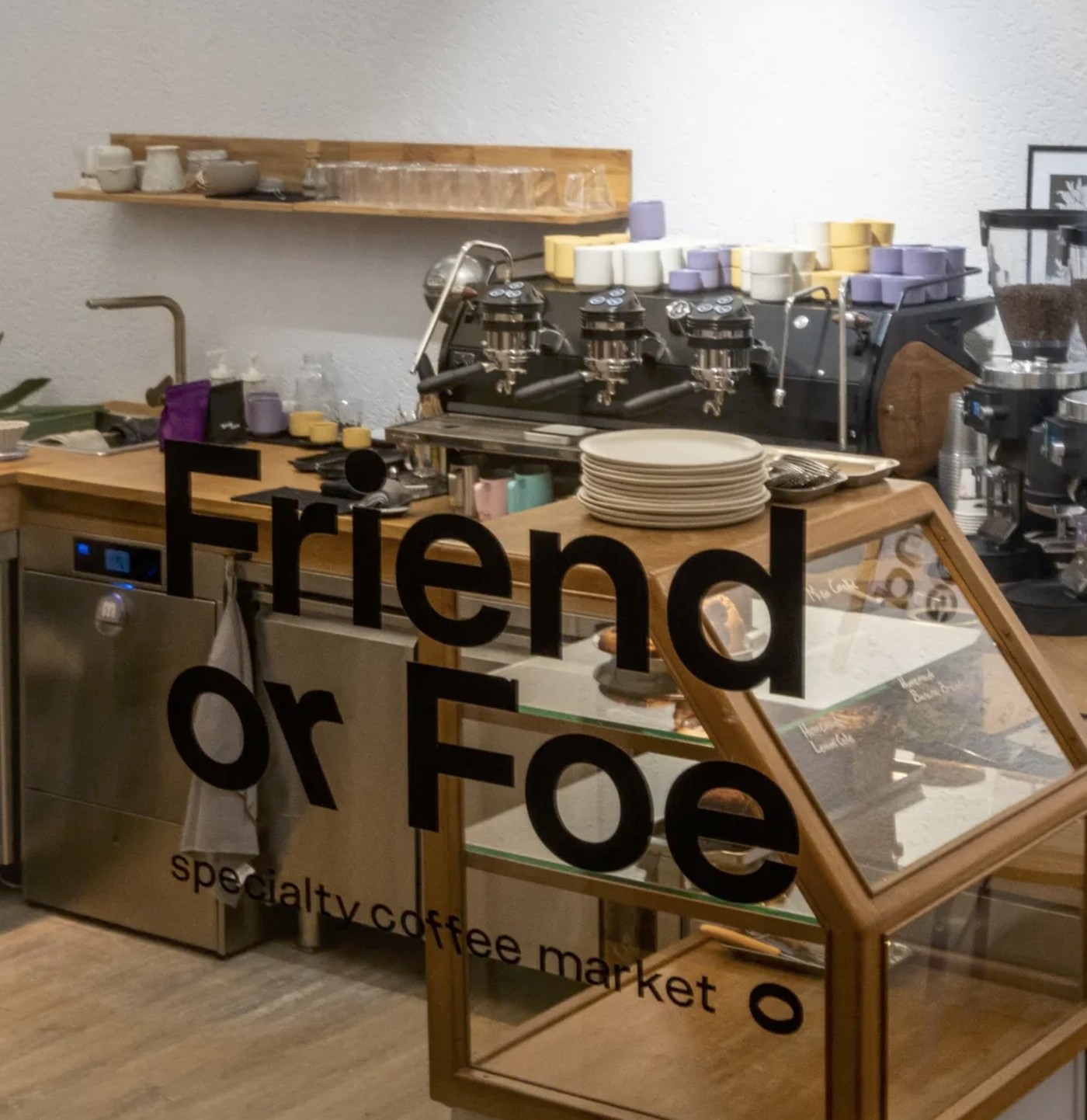 The Friend or Foe specialty coffee market logo painted on the window, with the espresso machine and pastry case visible behind it