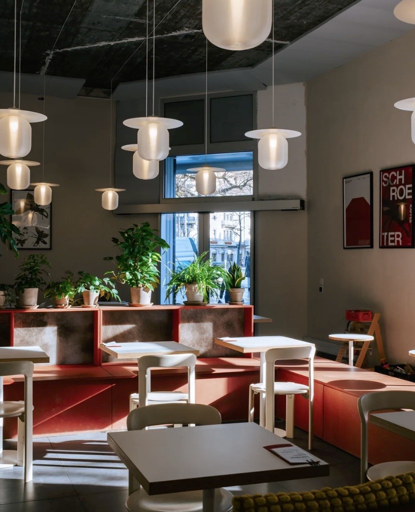 Globe pendant lights over terracotta booth seating and potted plants along the window at Schroeter Kaffee