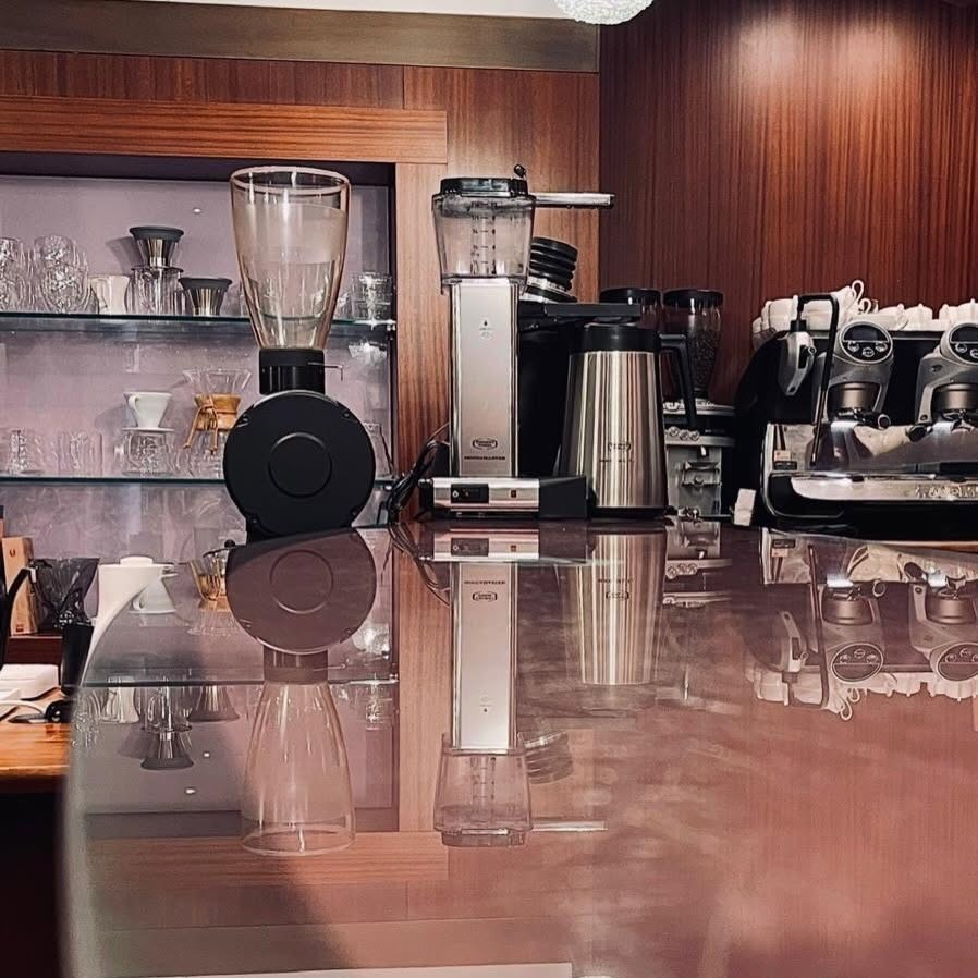 The polished Aroma counter with a pour over dripper, grinders, and a two group espresso machine reflected on the surface