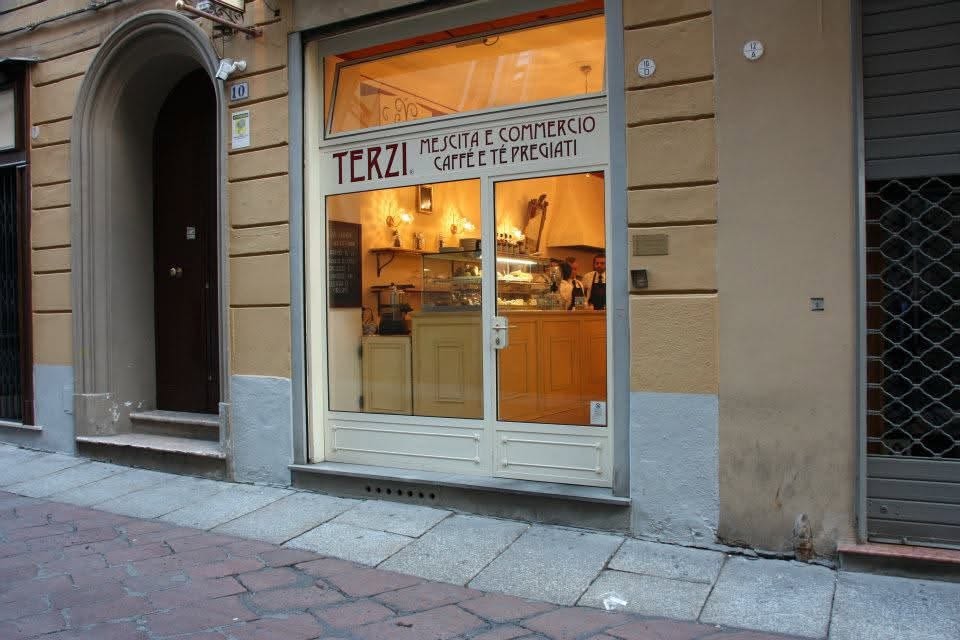 The illuminated Caffè Terzi storefront at dusk, with the Mescita e Commercio Caffè e Té Pregiati signage above the glass doors