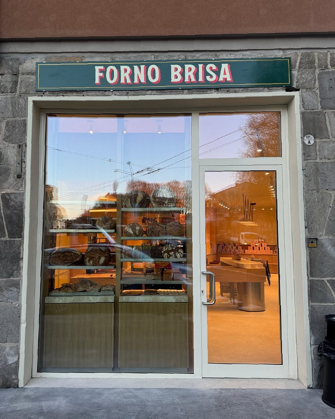 The Forno Brisa storefront window at dusk, with loaves of sourdough bread on display shelves