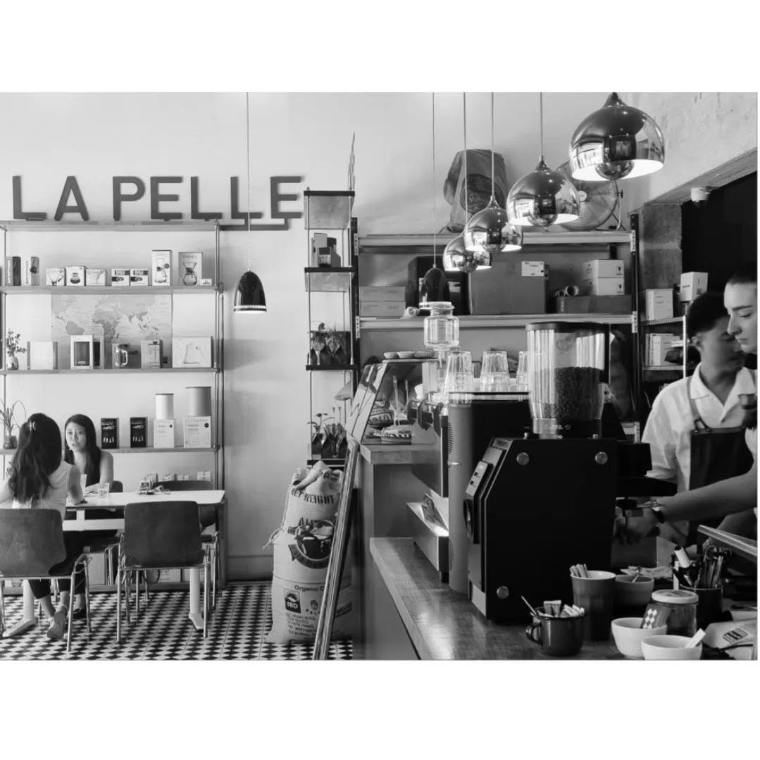 A black and white view of the La Pelle sign, retail shelves and world map on one side and the espresso bar with hanging globe lights on the other