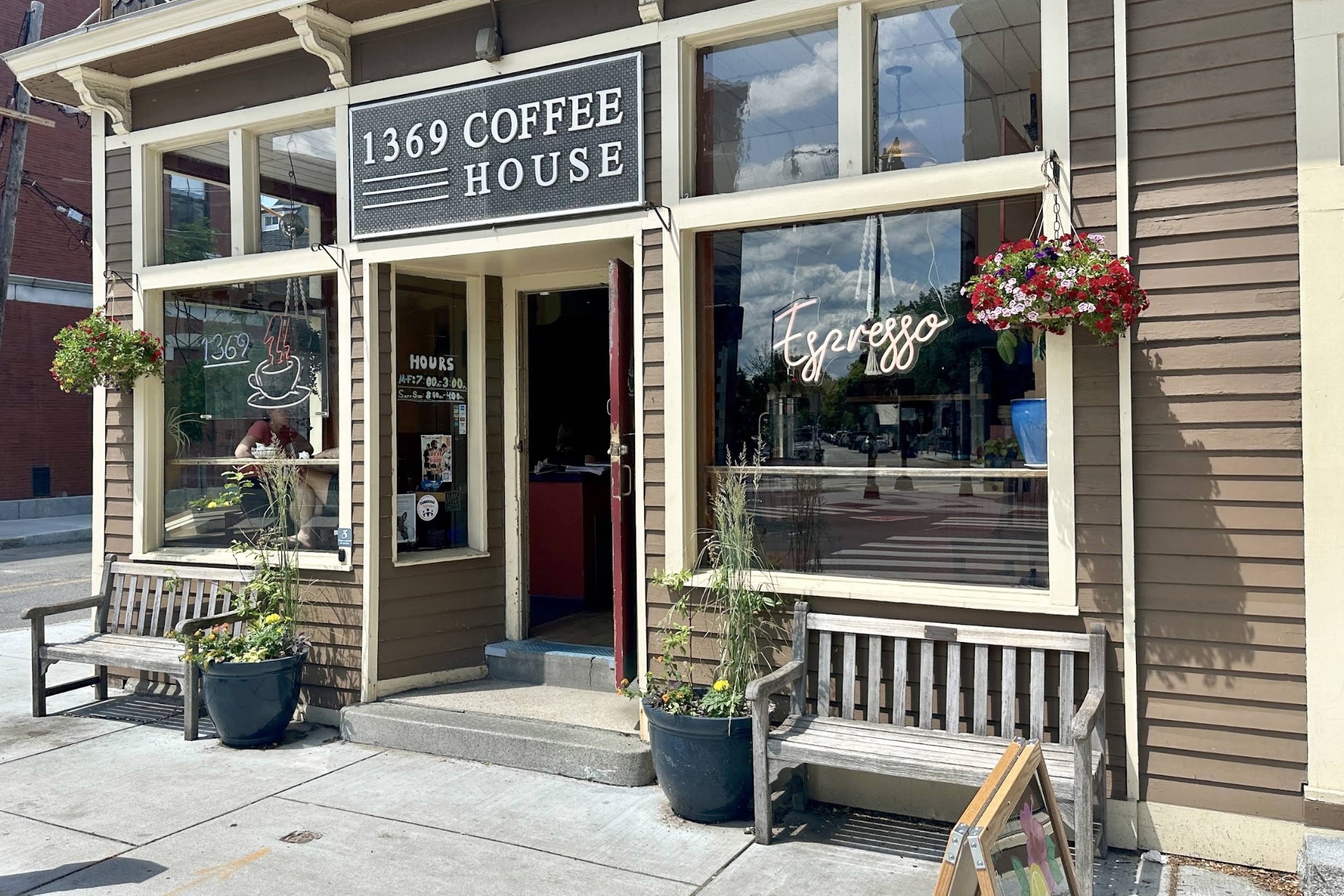 The 1369 Coffee House storefront with its sign, neon Espresso window and hanging flower baskets over sidewalk benches