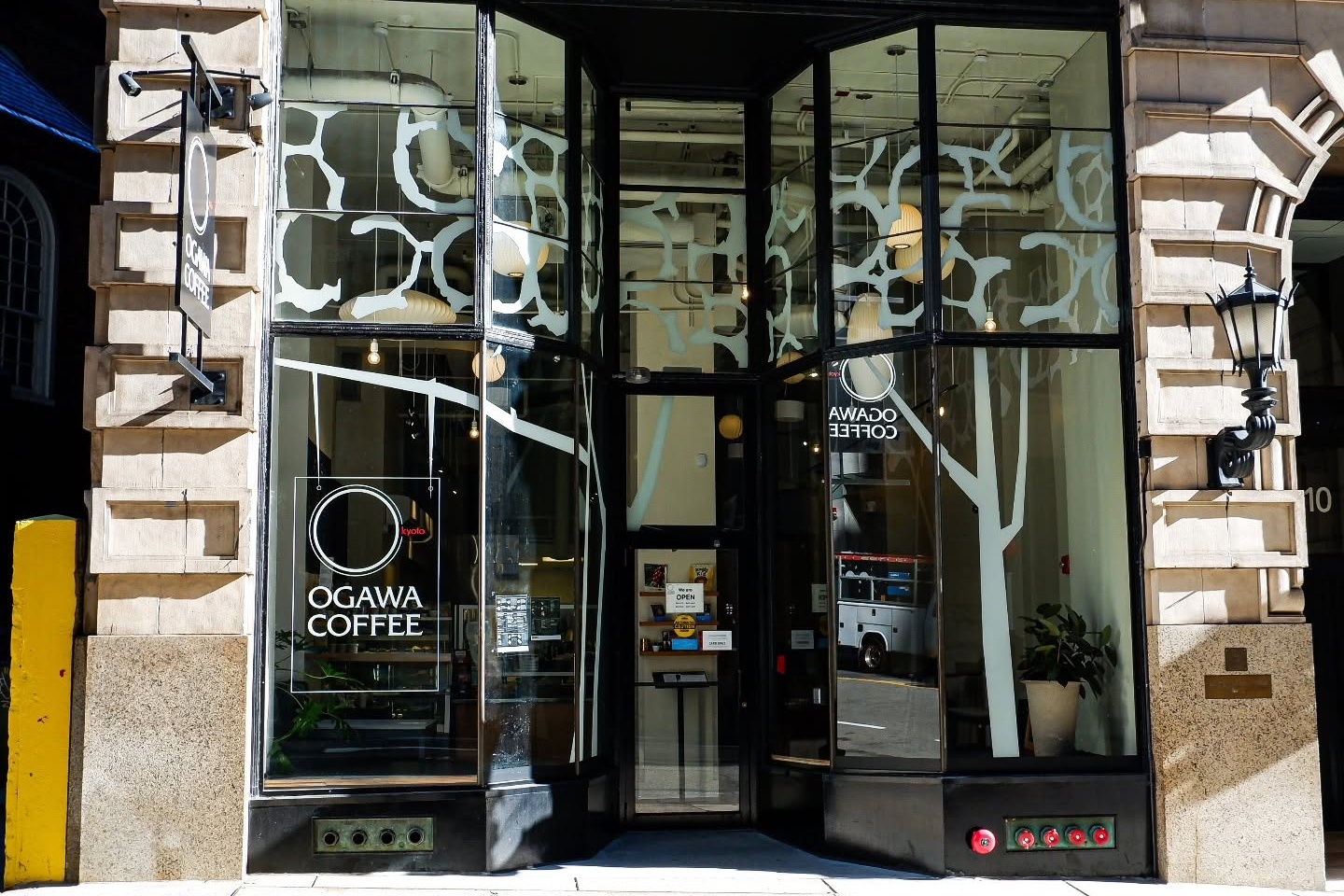 The Ogawa Coffee storefront on Milk Street, its tree branch window decals and hanging pendant lights visible through the glass