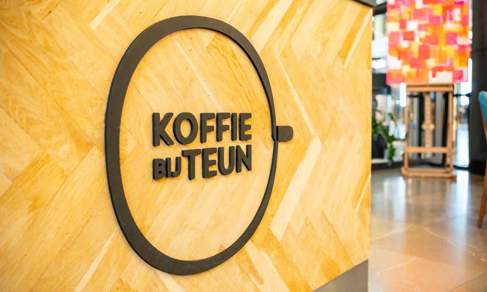 The KOFFIE BIJ TEUN logo mounted on a herringbone wood wall