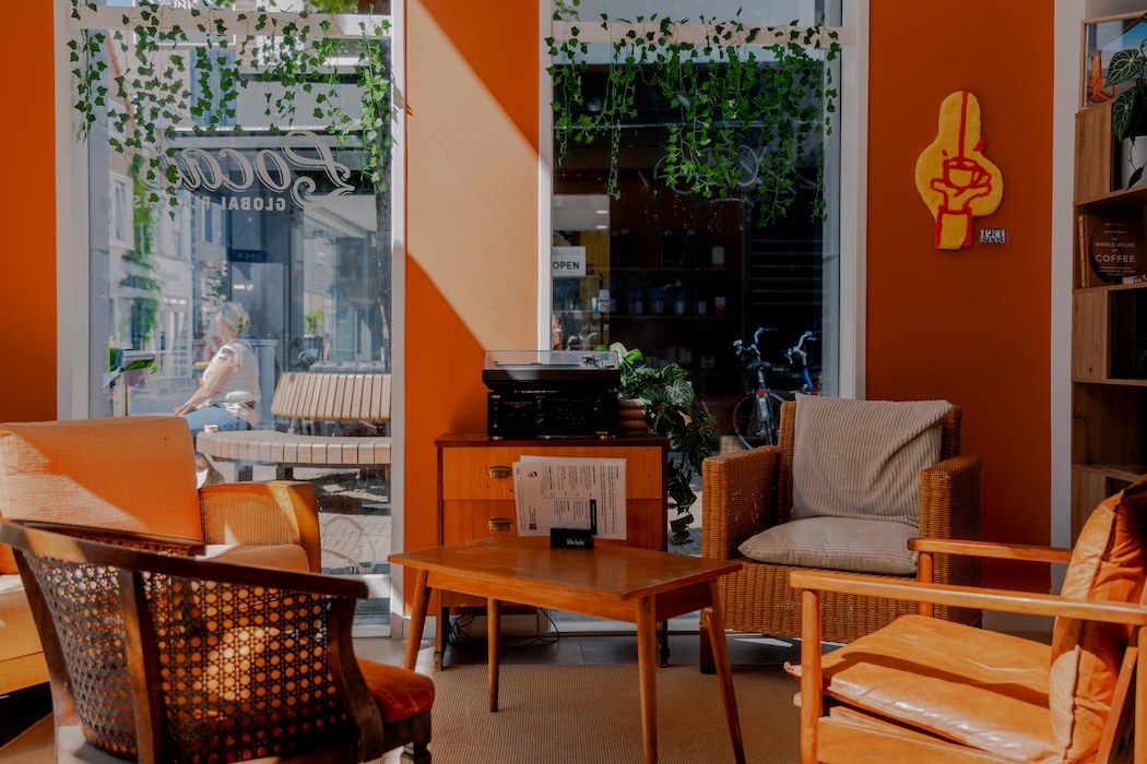 A warm orange lounge corner with rattan armchairs, a record player and trailing plants, storefront glass visible behind