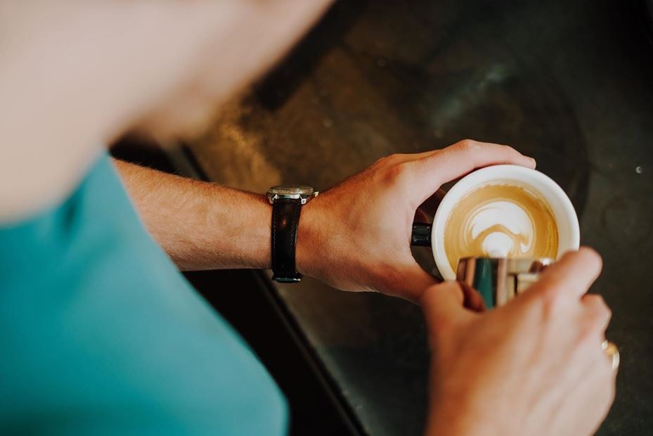 A cappuccino with latte art held in hand over a dark table