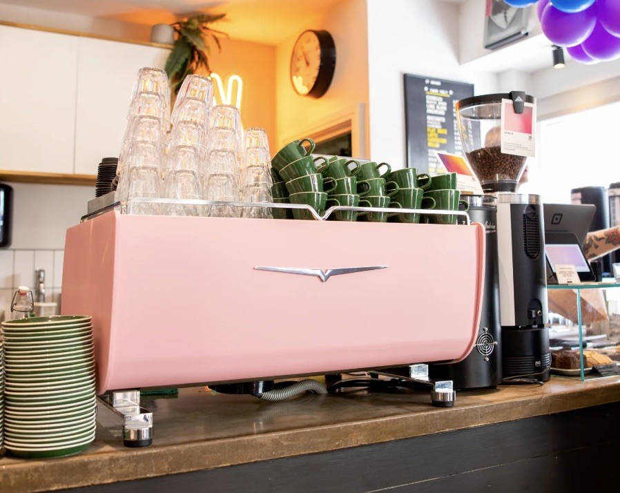 A pink vintage style espresso machine stacked with glasses and green cups on the counter at 17 GRAMS