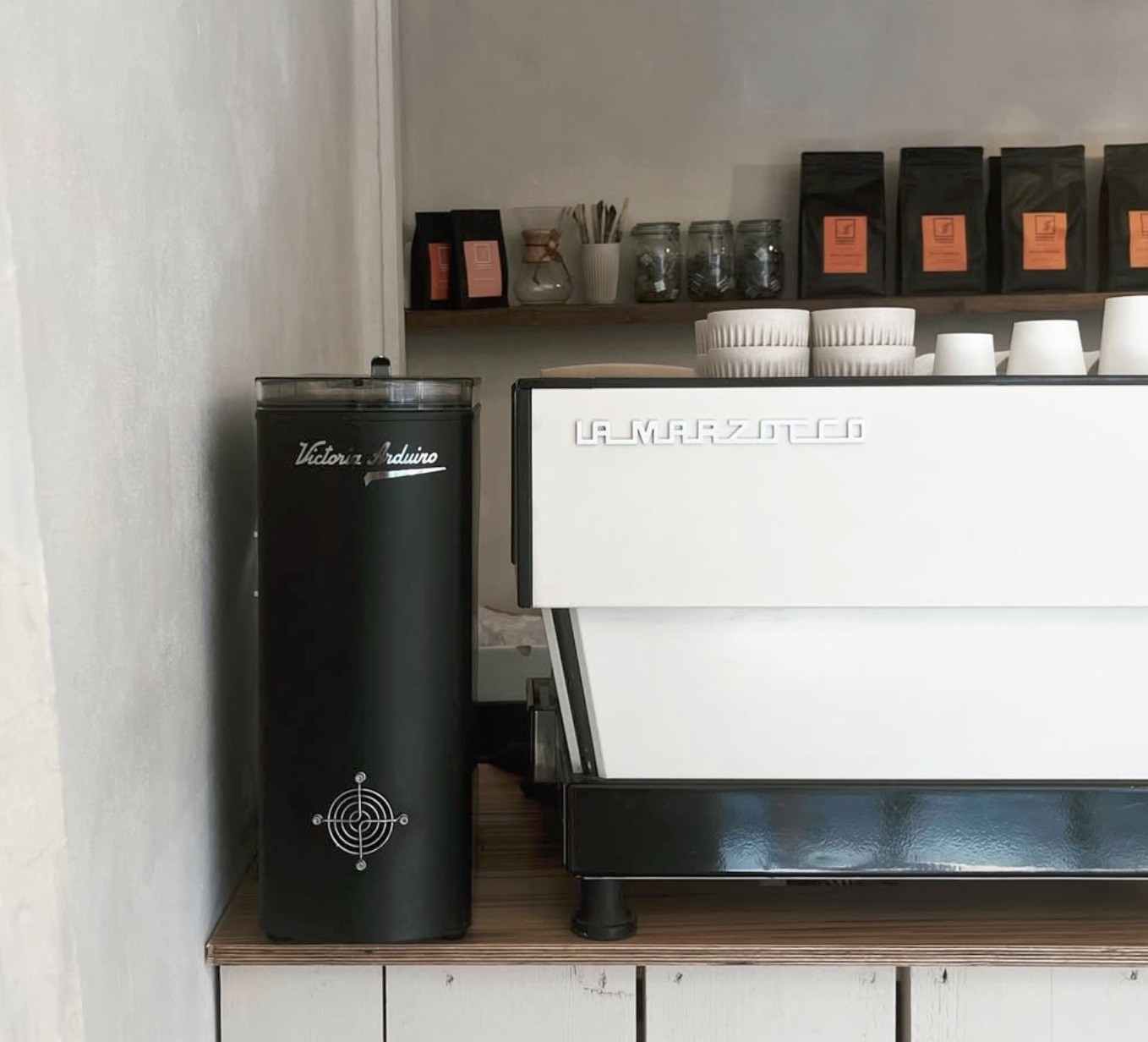 A La Marzocco espresso machine and Victoria Arduino grinder beneath a shelf of retail coffee bags at Dandy
